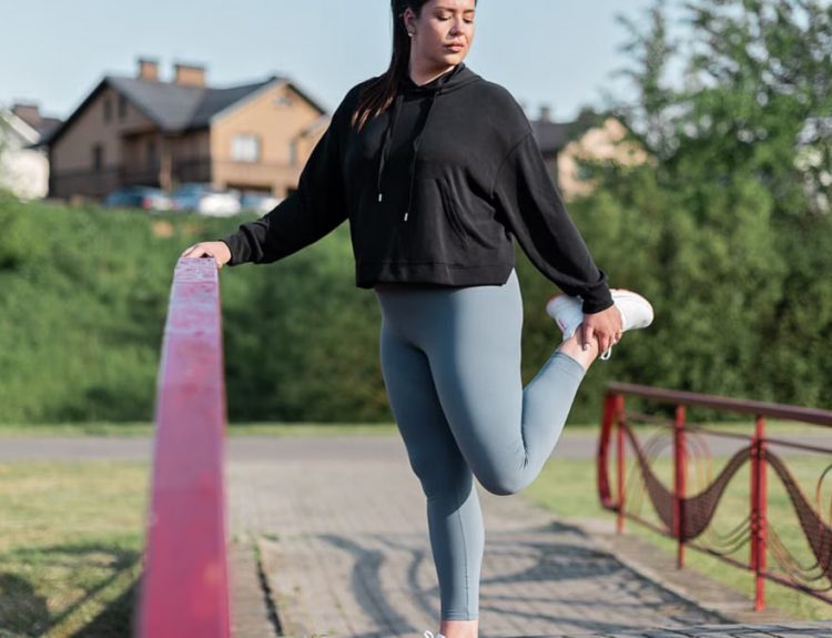 Young woman in activewear stretching on a red railing outdoors.